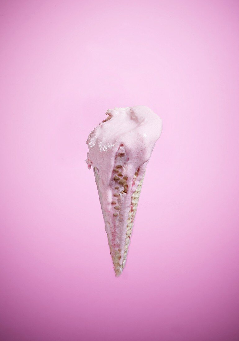 An ice cream cone with melting strawberry ice cream