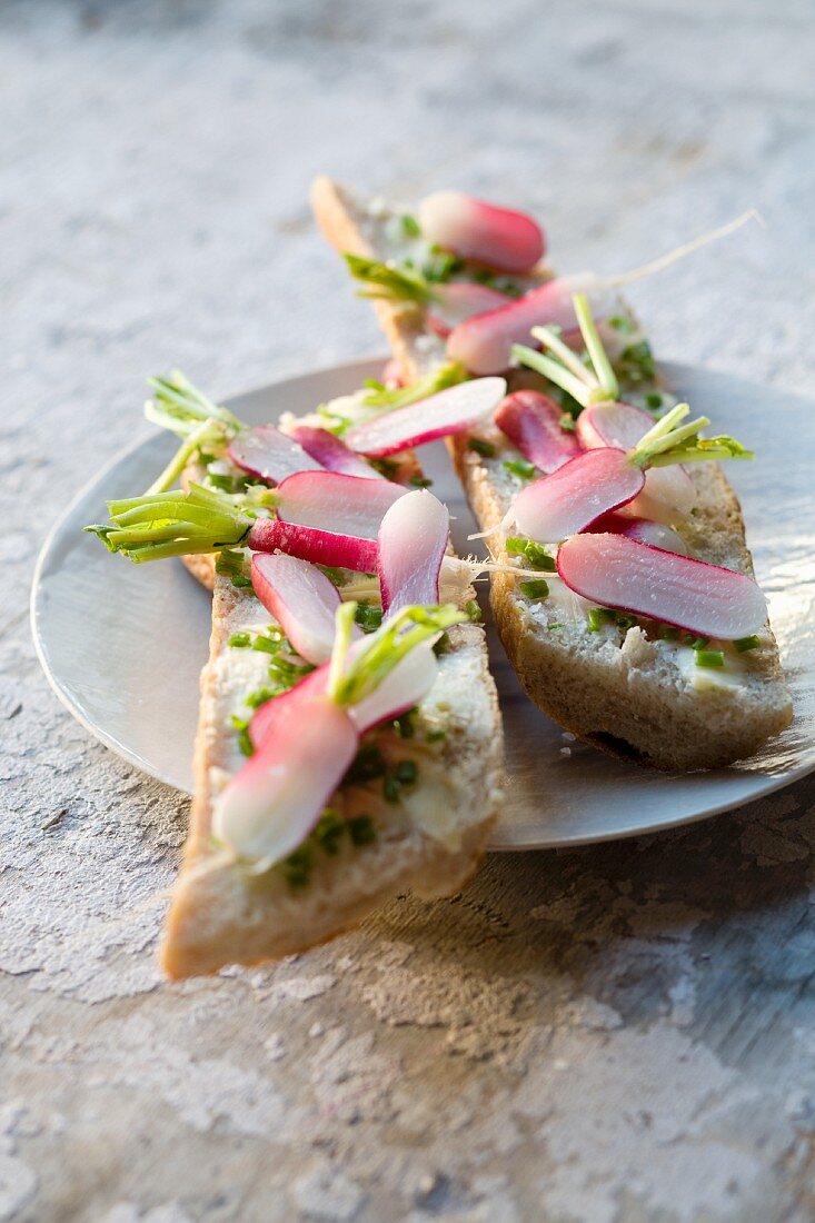 Slices of bread and butter topped with radishes and chives