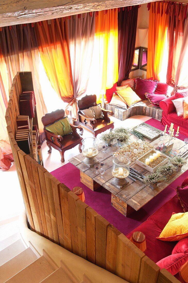 View from staircase into lounge area with wooden partition and large DIY table with candelabra in front of windows with sunlight shining through closed curtains