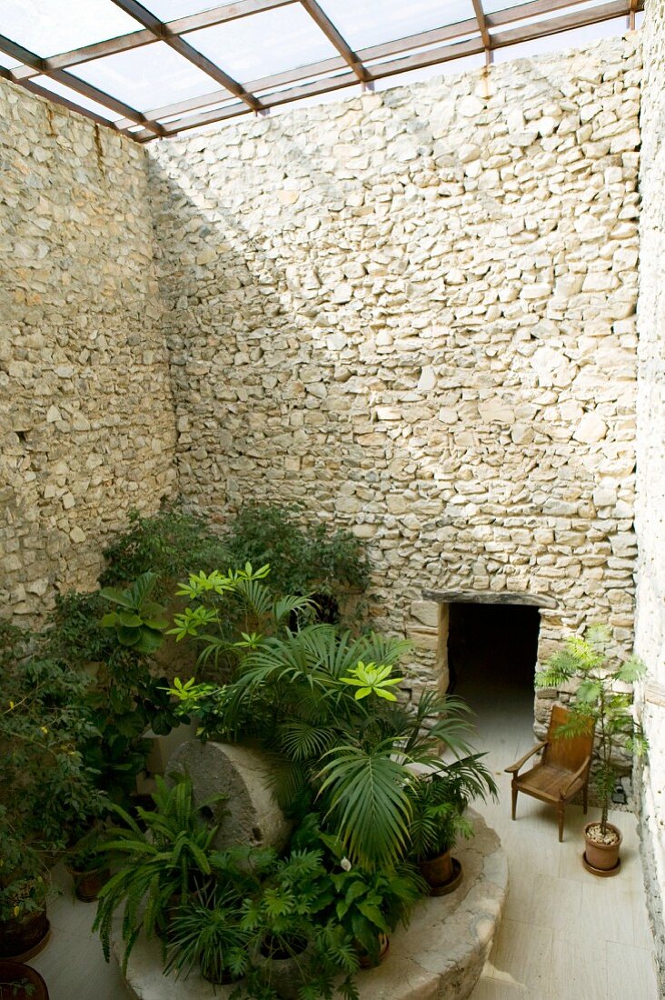 Grüne Pflanzen und ein Holzstuhl, umgeben von den hohen Natursteinmauern eines glasüberdachten Innenhofs