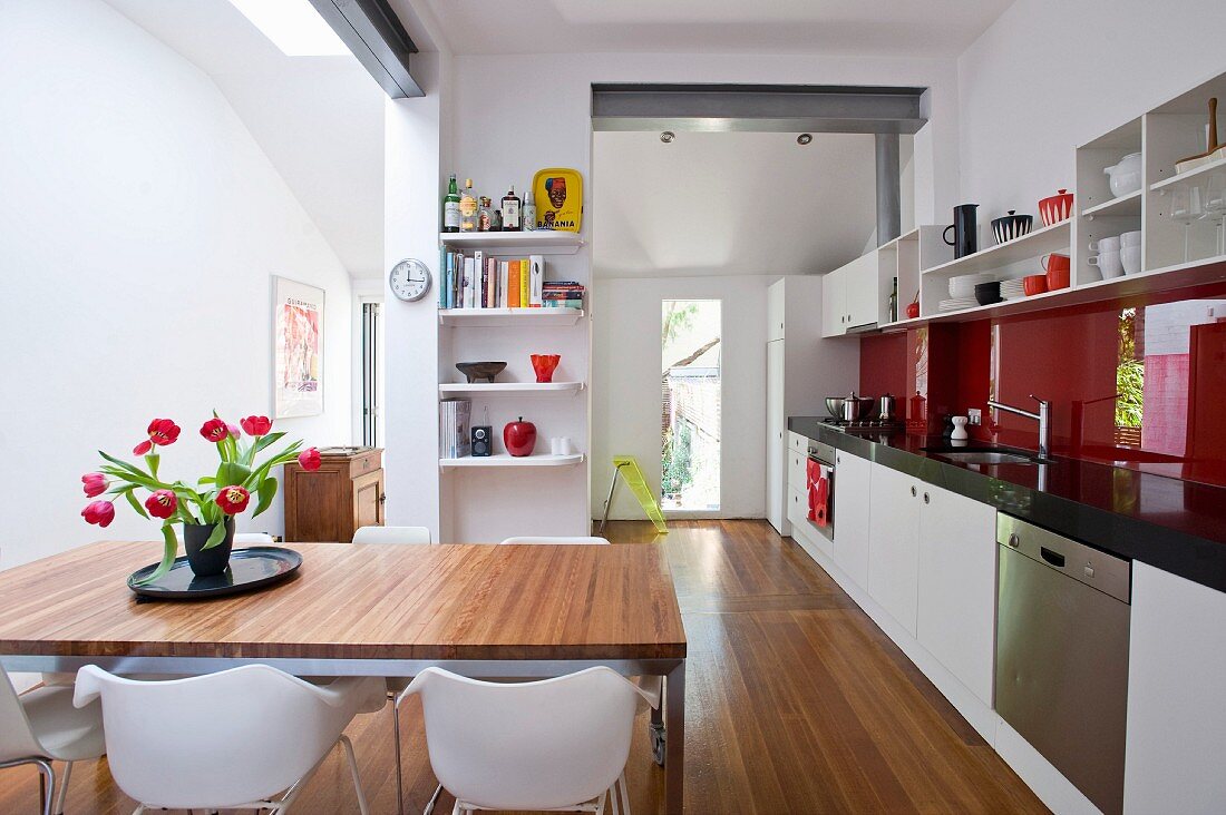 Bouquet of tulips on dining table in modern, open-plan kitchen with long kitchen counter and red glass splashback