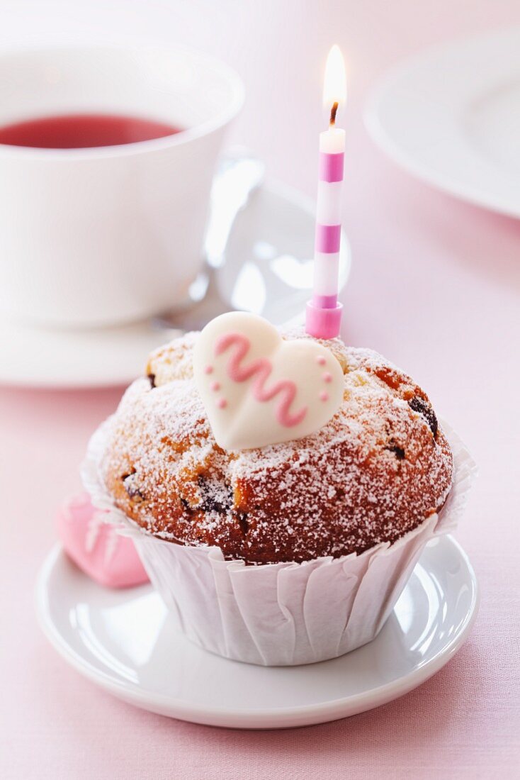 A muffin decorated with a candle and a sugar heart