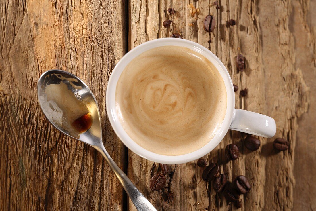 Eine Tasse Espresso mit Löffel und Kaffeebohnen auf Holzuntergrund