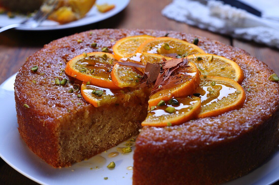 An orange cake topped with pistachios, with one slice missing
