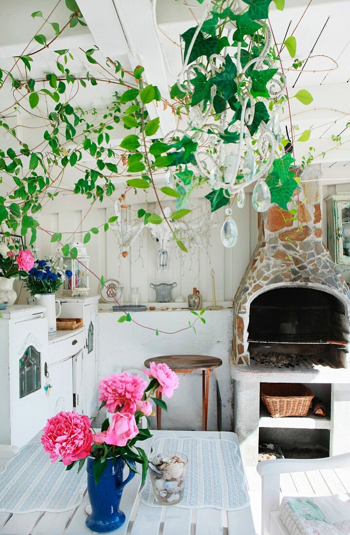 Vase of pink peonies on garden table in white wooden veranda with fireplace