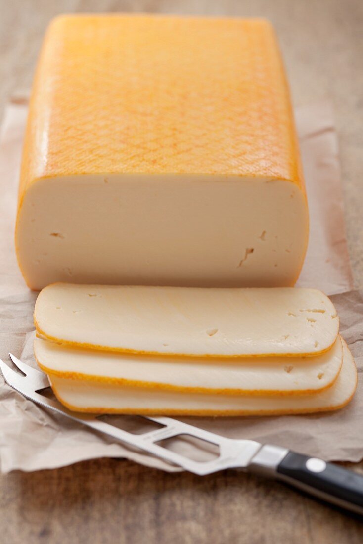 Butterkäse (mild, semi-soft cheese), partly sliced, on paper with a cheese knife