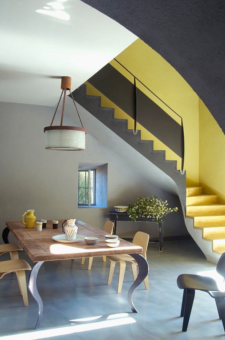 Designer table and wooden chairs in front of anthracite interior staircase