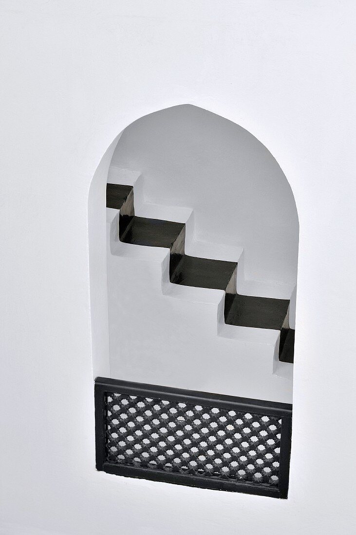 Blick durch orientalische Maueröffnung mit Holzbrüstung auf das schwarze Läuferband eines schmalen Treppenaufgangs