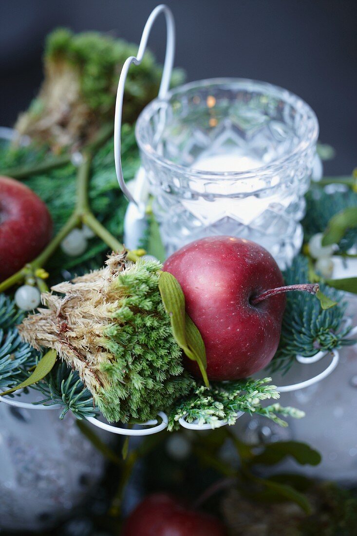 Christmas arrangement on cake stand with apples, fir branches, mistletoe, moss, tealight and baubles