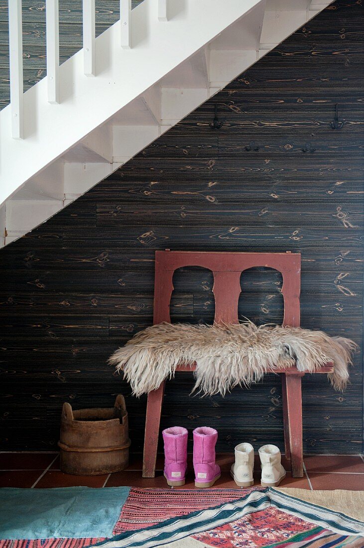 Sheepskin on chair and children's' boots against wooden wall in alcove below staircase