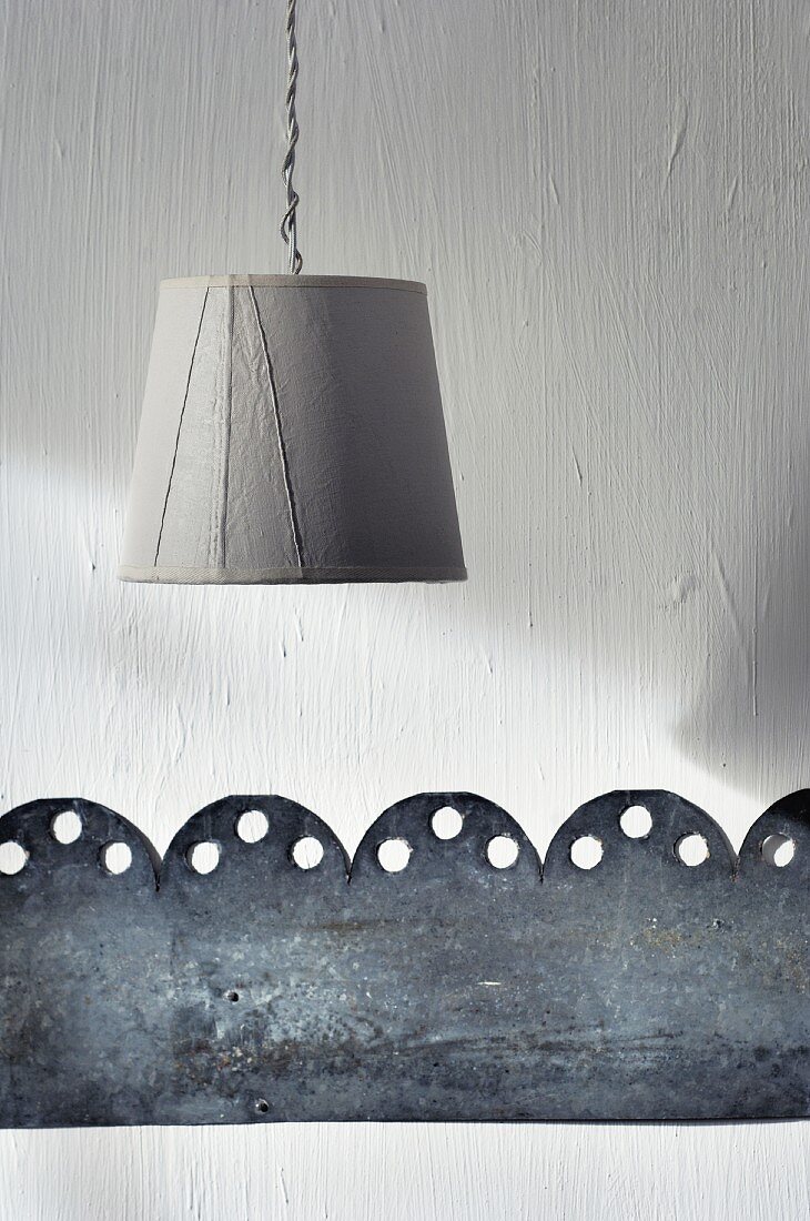 Schlichter Lampenschirm und ausgestanzter Blechstreifen als minimalistische Wandverzierung