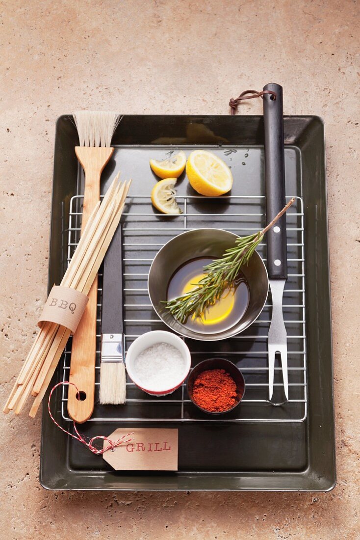 Assorted barbecue utensils, seasonings, lemons and olive oil on a barbecue grill