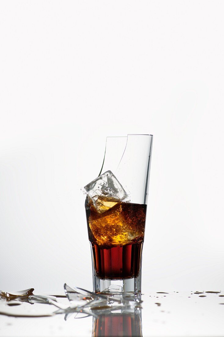 A broken glass with cola and ice cubes