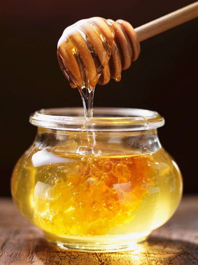 Honig tropft vom Honiglöffel in ein Glas