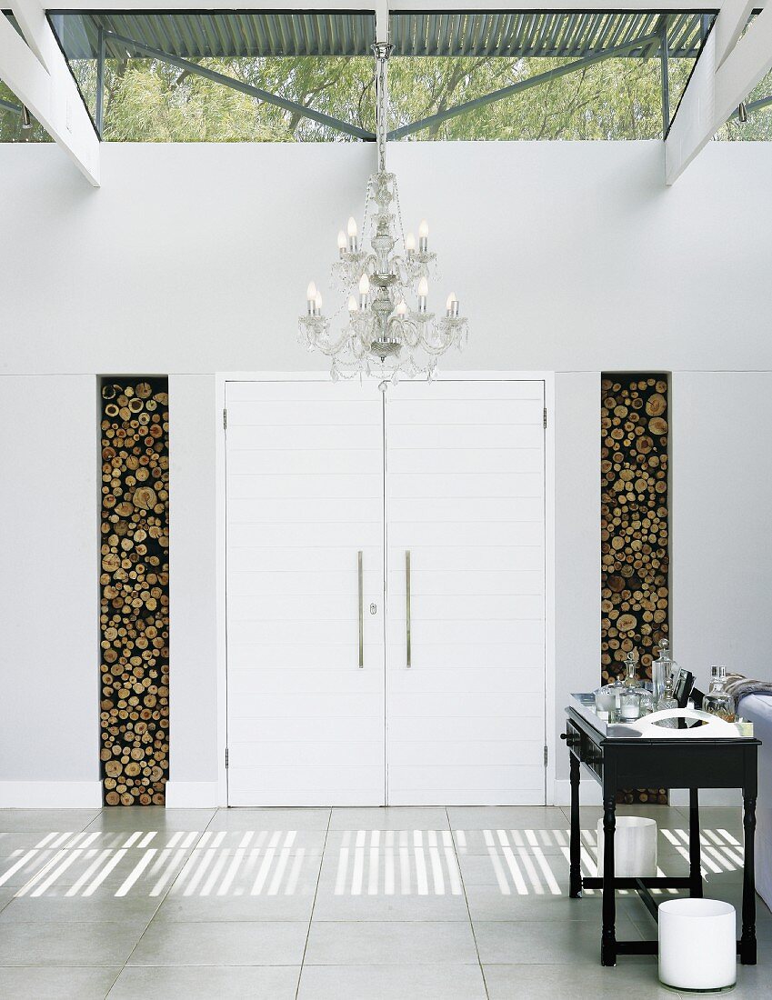 Classic chandelier under modern steel construction in the lobby; wall niches for firewood on both sides of the double entry door