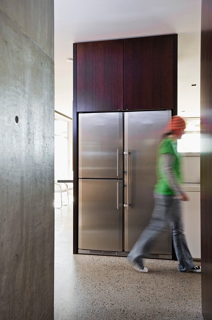 Open floor plan in a puristic home with exposed concrete walls - person running in front of a built in, stainless steel refrigerator