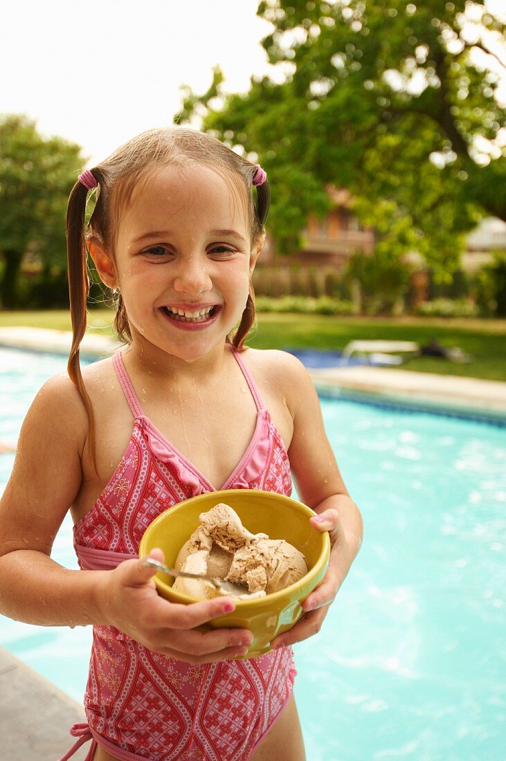 Kleines Mädchen mit einer Schale Eis neben einem Pool