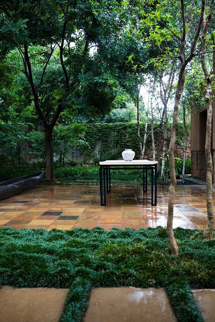 Tropical garden: vase on table on tiled terrace, wet and glossy with rain