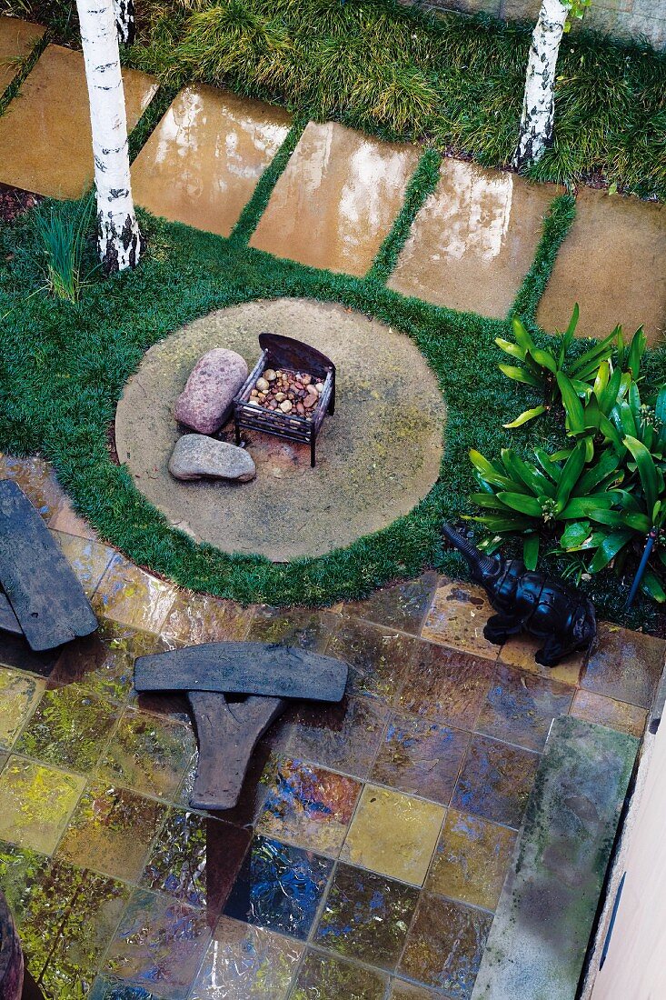 Gestalteter Garten mit Feuerstelle auf Kreisfläche und Kunstobjekte auf gefliestem Terrassenboden