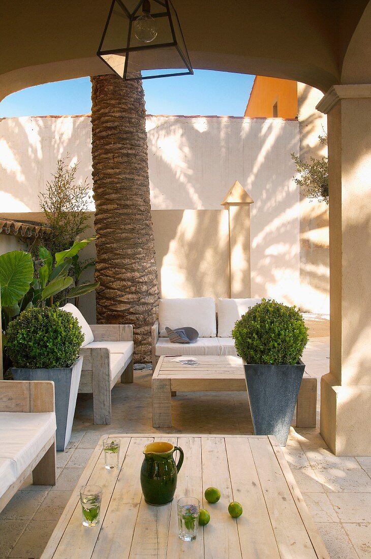 Mediterranean veranda with planters amongst wooden outdoor coffee tables and matching benches