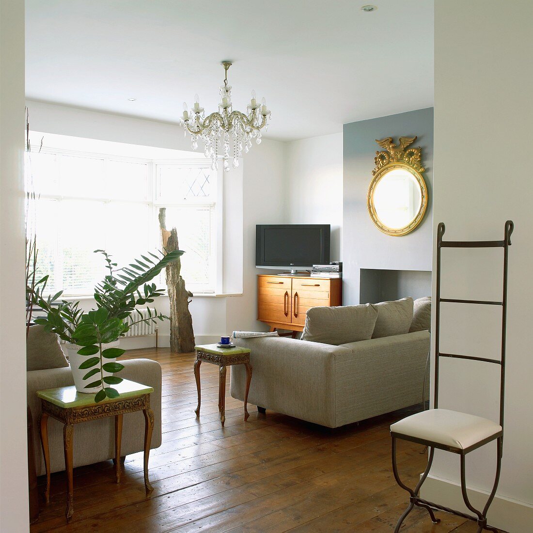 Mix of furniture styles in a living room with delicate wrought iron chair and rococo style side tables next a modern upholstered sofa