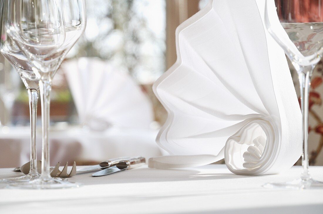 Kunstvoll gefaltete weiße Stoffserviette auf gedecktem Tisch