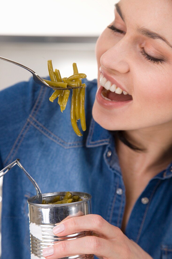 A woman eating green beans from the tin