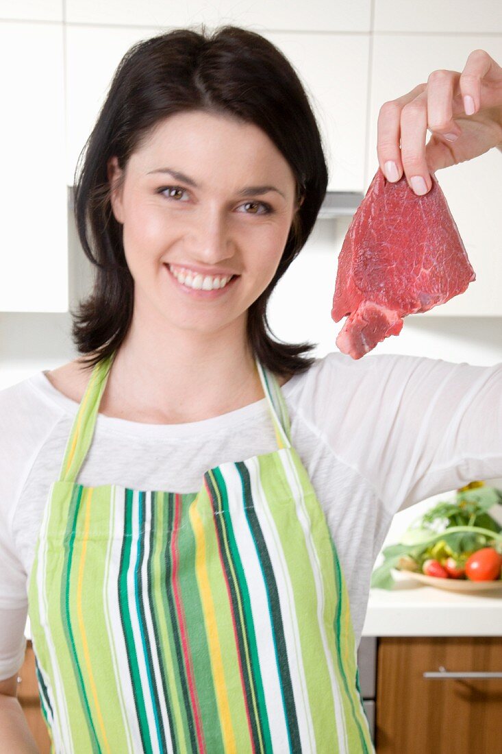 A woman holding up a raw steak in the kitchen