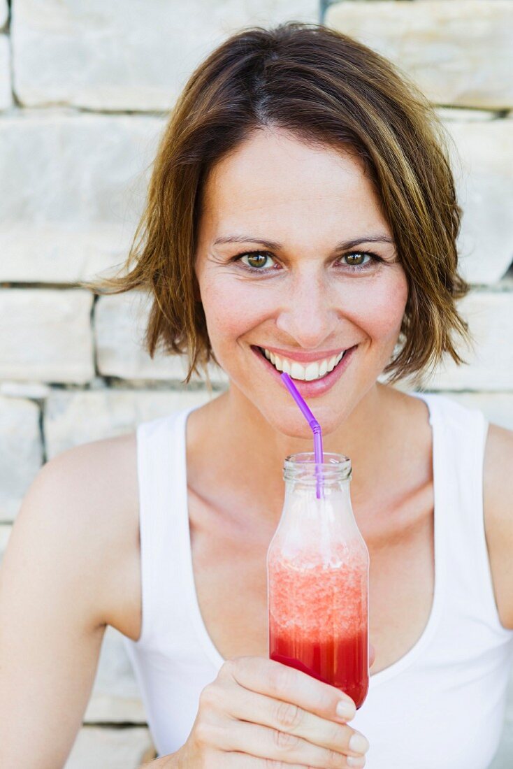 A smiling woman drinking a smoothie from a bottle