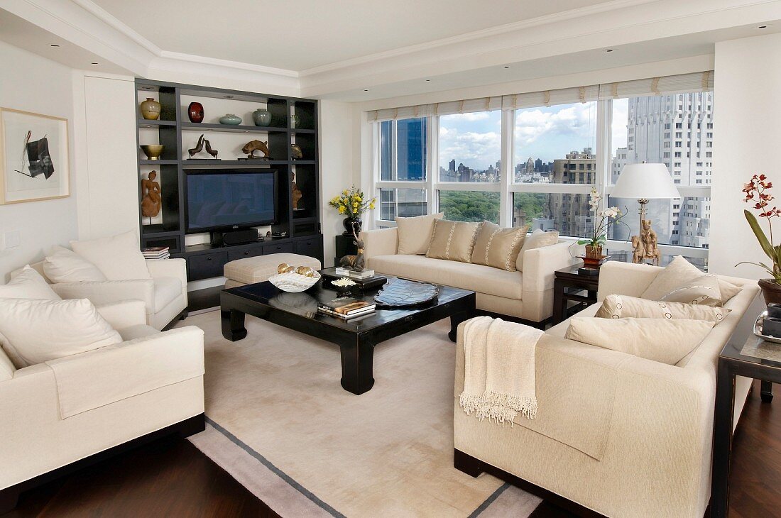 Sofa set with pale upholstery around dark wood coffee table in front of fitted shelving and panoramic window