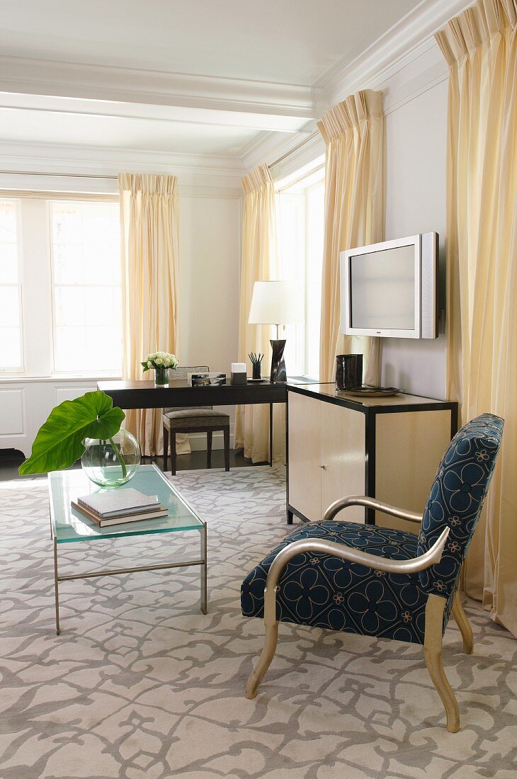 Sessel vor Glastisch auf gemustertem Teppich in klassischem Wohnzimmer mit hellgelben bodenlangen Vorhängen am Fenster