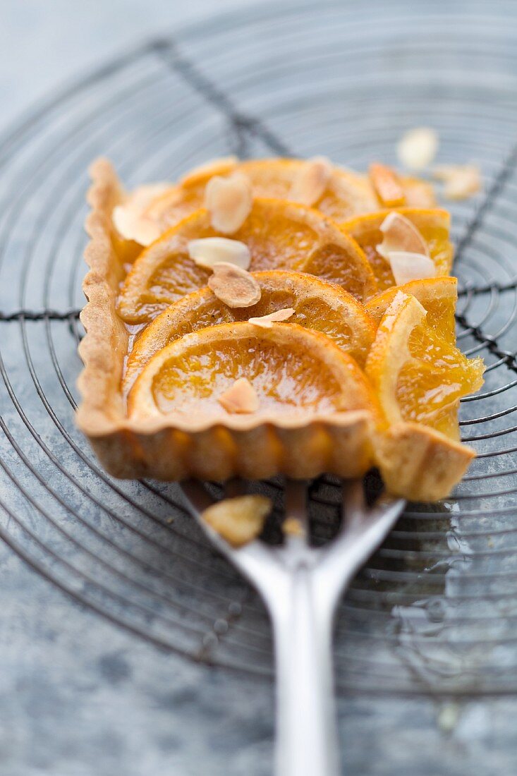 A piece of orange tart with slivered almonds on a spatula