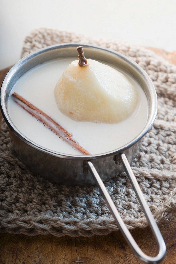 A poached pear in coconut milk with a cinnamon stick