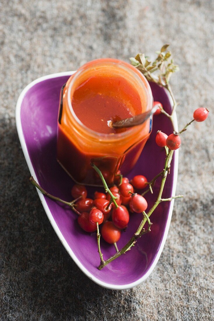 A jar of rose hip jelly and fresh rose hips