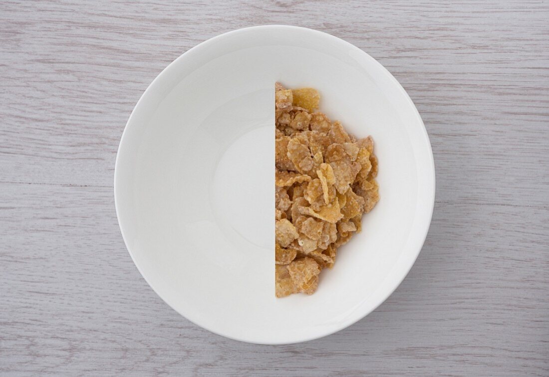 Halbierte Portion Cornflakes in weisser Schale (Aufsicht)