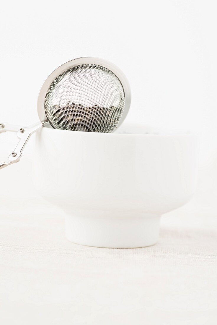A tea strainer balanced on a white tea bowl