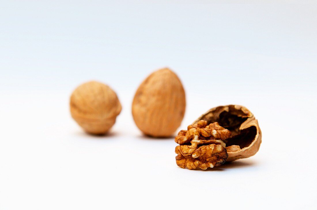 Three walnuts; two whole, one with the shell broken open