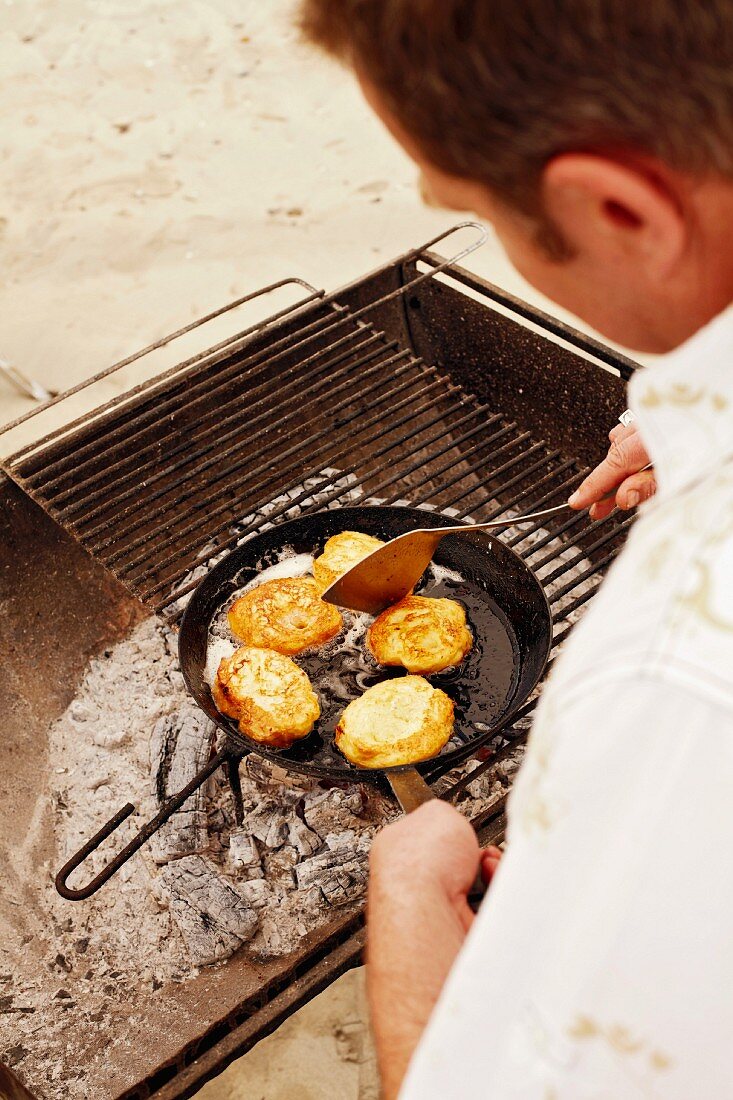 Baguette slices coated in egg yolk being fried in a pan on a barbecue