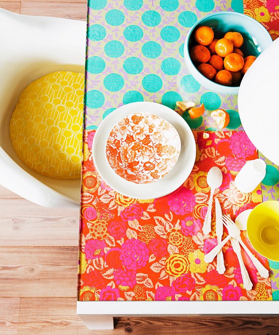 Glass table hand-decorated with hippie-style, colourful floral wrapping paper; retro shell chair with yellow seat cushion