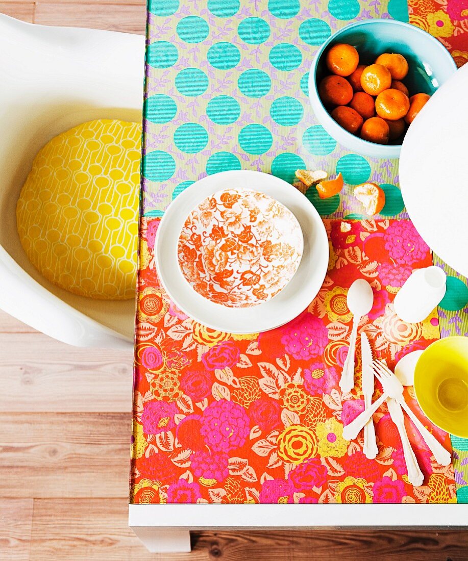 Im Hippie-Look, farbenfroh mit floral gemustertem Geschenkpapier selbst gestalteter Glastisch; Retro Schalenstuhl mit gelbem Kissen