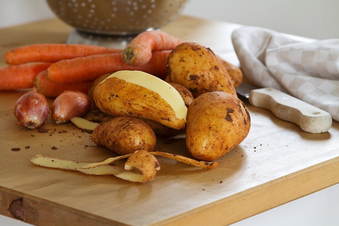 Karotten, Schalotten und Kartoffeln; eine davon geschält
