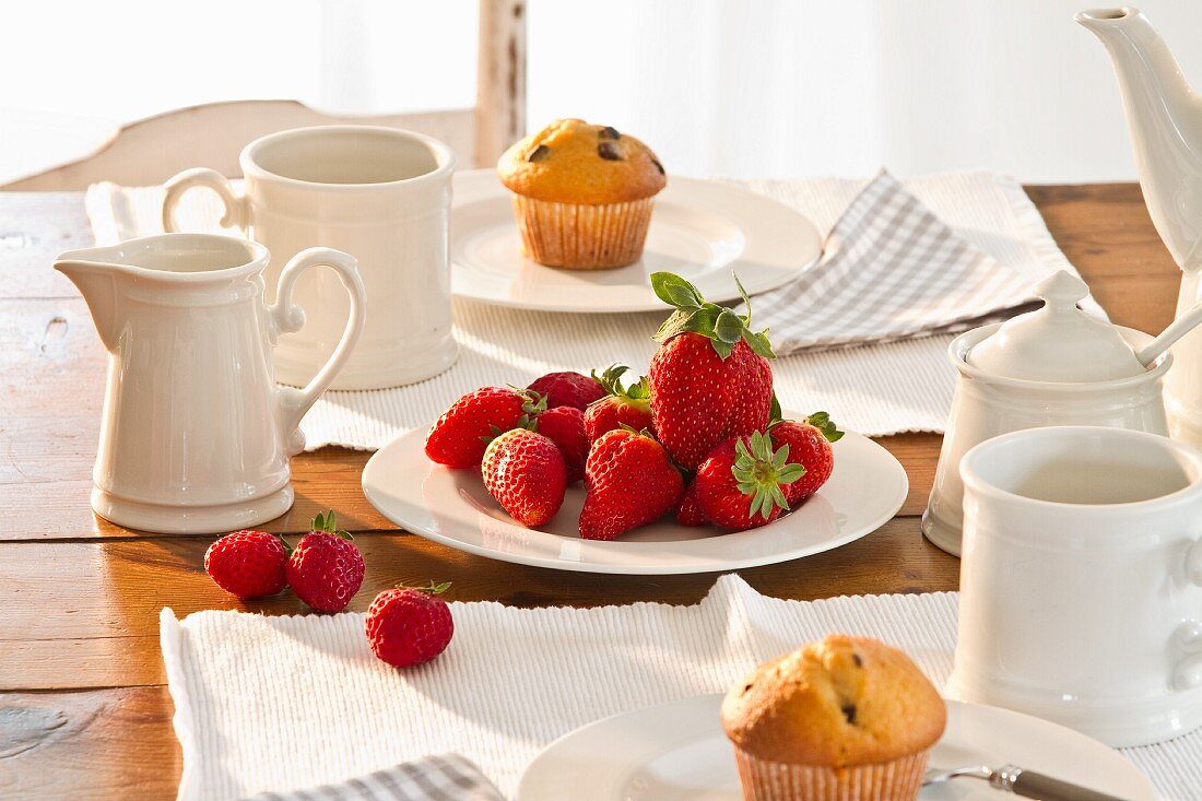 A table laid for coffee with muffins and fresh strawberries
