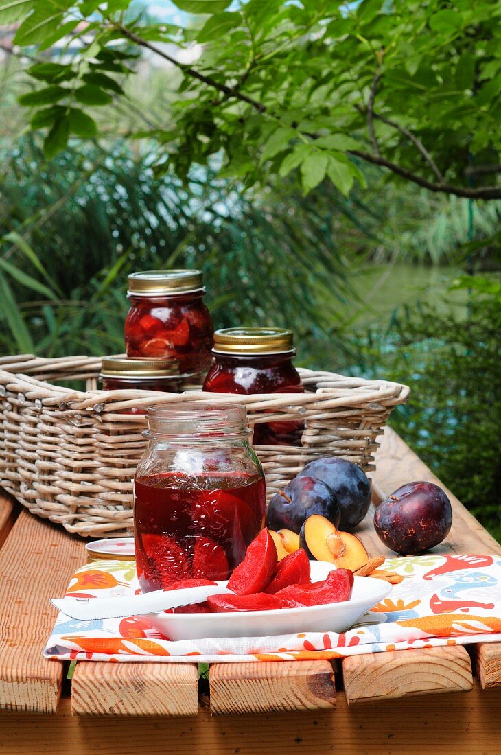Rum plums in preserving jars and on a plate, on a table in the garden