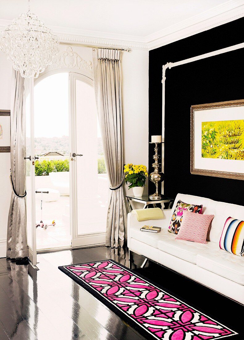 Rug with pink and white geometric pattern on black wooden floor in front of white couch and black wall in corner of living room