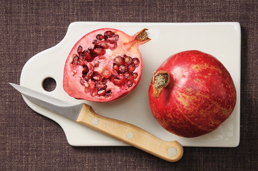 Ganzer und halber Granatapfel auf Schneidebrett mit Messer
