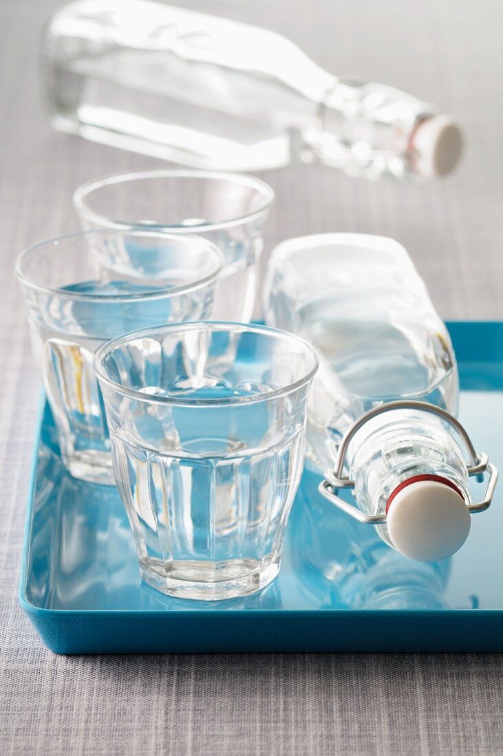 Three glasses of water and two bottles of water, some of these on a blue tray