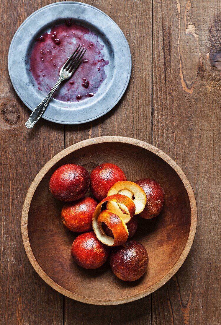A Wooden Bowl of Blood Oranges with Peel; Dirty Plate with a Fork; From Above