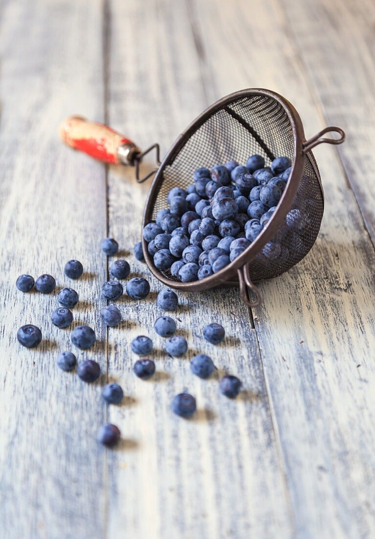 Fresh Blueberries Spilling From an Old Strainer onto a Wooden Table