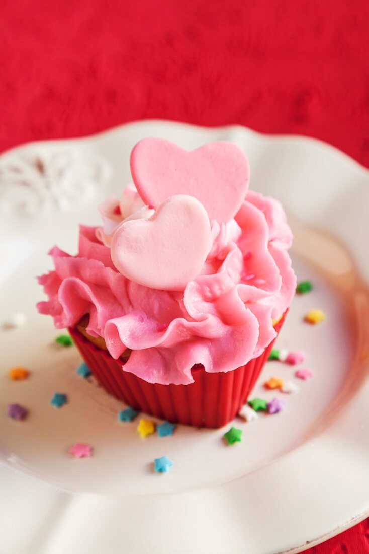 Pink Frosted Cupcake with Pink Hearts and Confetti Sprinkles; On a White Plate