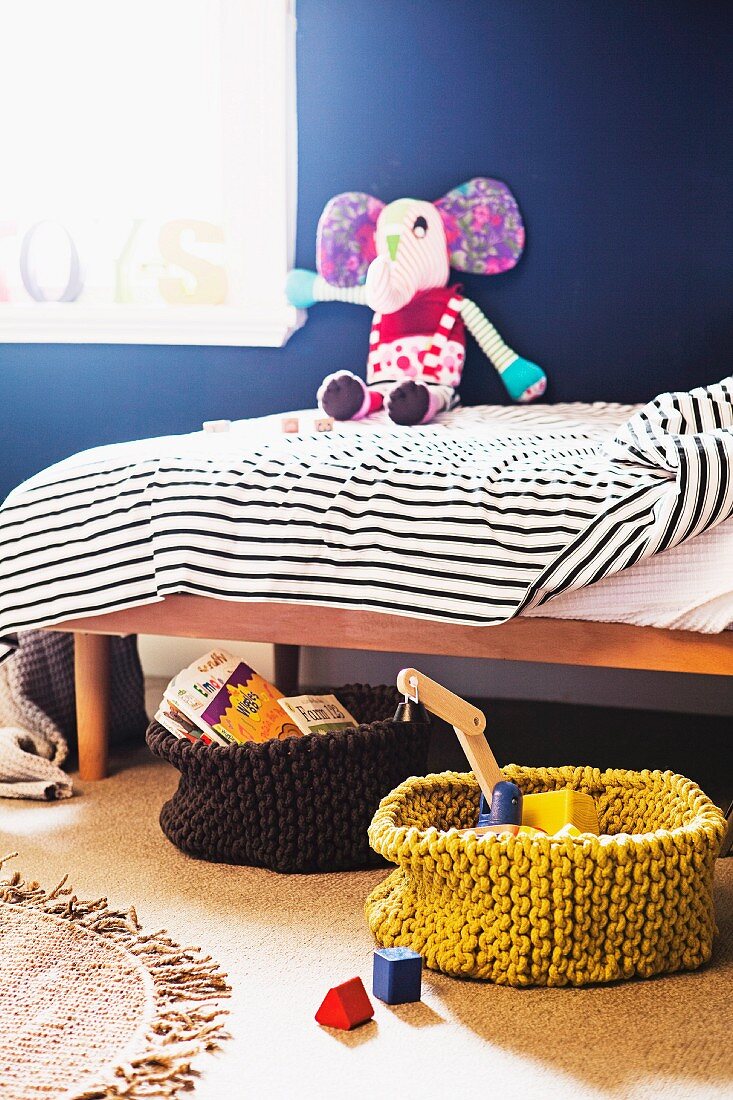 Spielzeuge und Bücher in Strickkörben vor Kinderbett mit Stofftier
